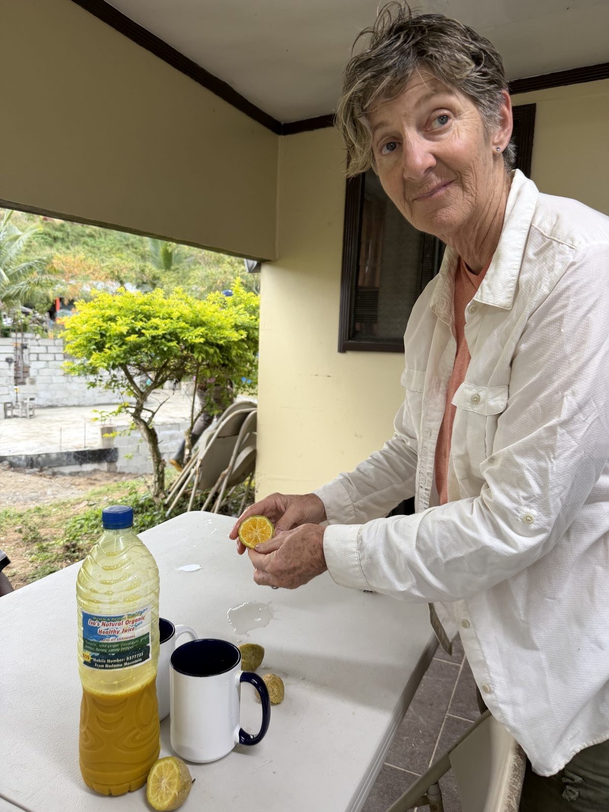 Whitney squeezing fresh citrus into a mug beside a bottle of Iva's Natural Organic Healthy Juice from the local street market in Fiji.