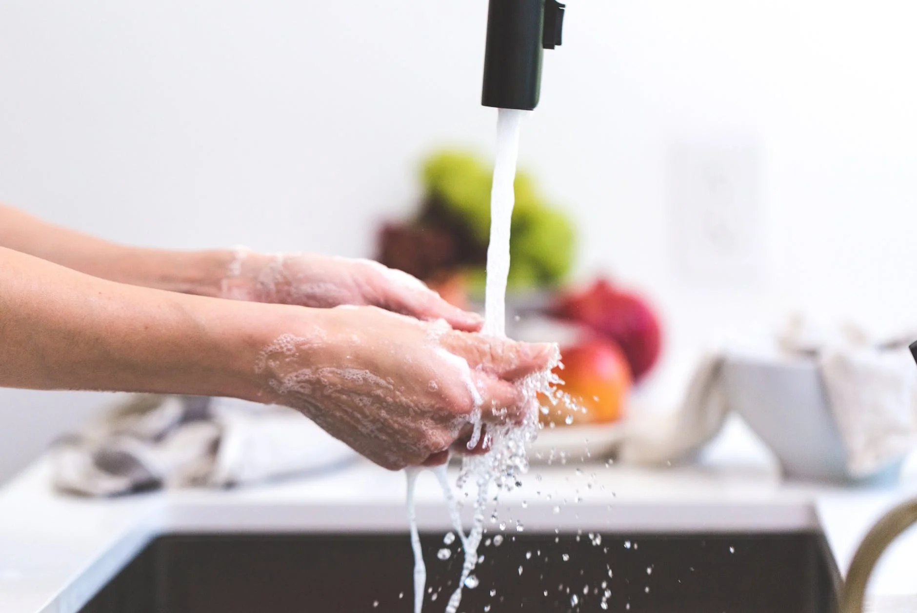 Hands washing fresh produce at a kitchen sink